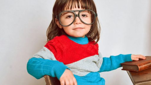 girl in red framed eyeglasses and gray sweater sitting on brown wooden chair