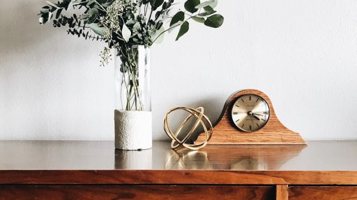 brown wooden framed analog mantle clock near gray petaled flower centerpiece