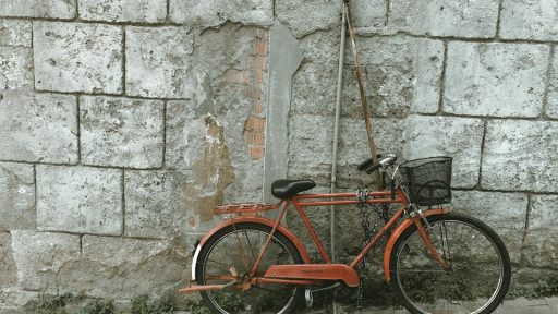 An old red bicycle leaning against a weathered concrete wall, offering a vintage urban appeal.
