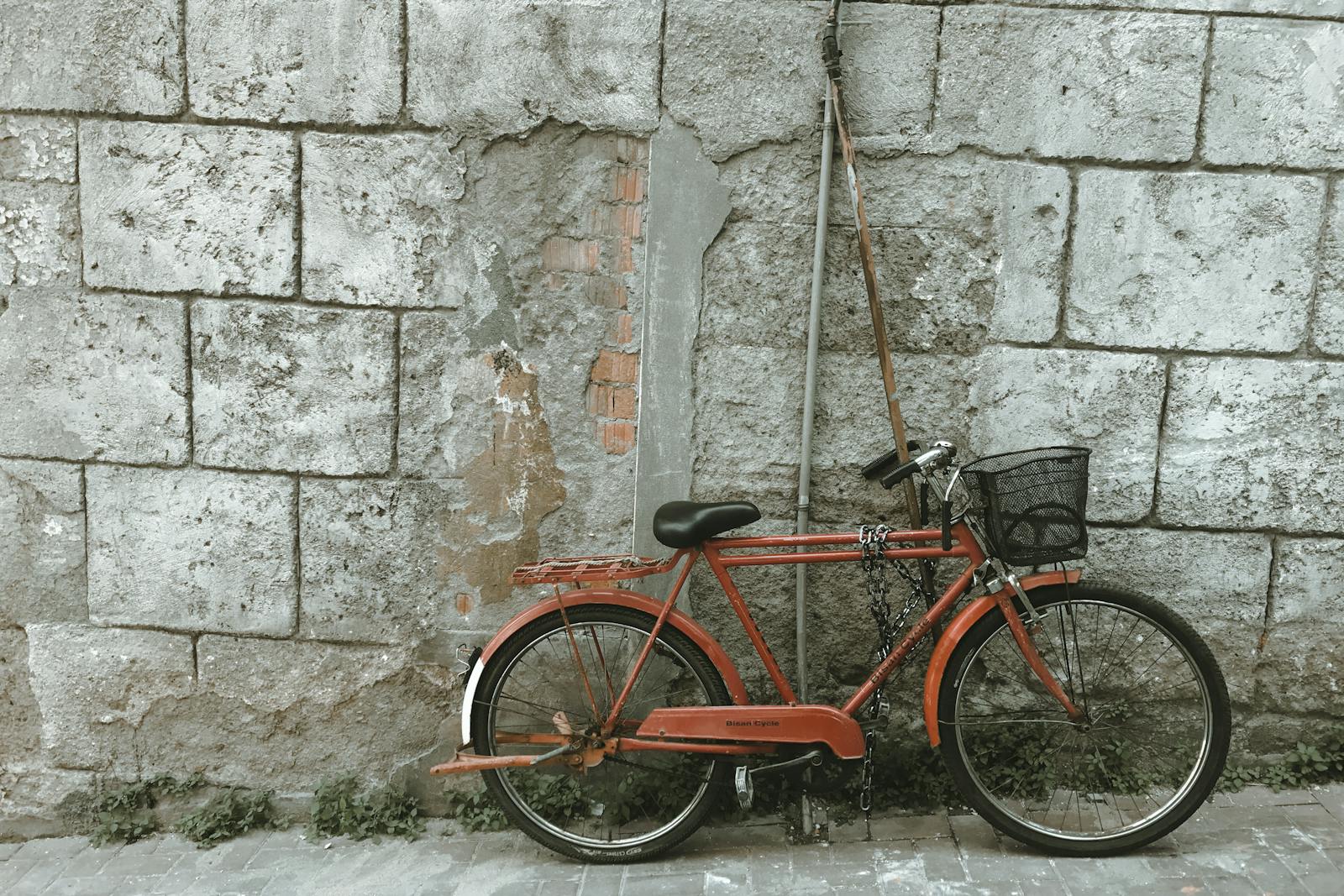 An old red bicycle leaning against a weathered concrete wall, offering a vintage urban appeal.