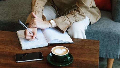Vrouw schrijft in notitieboekje aan tafel met koffie