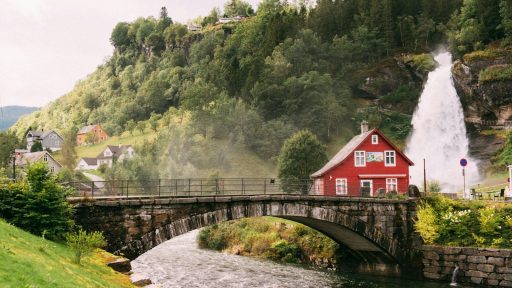 A red house beside a waterfall and stone bridge in a green valley