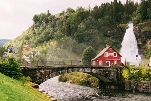 A red house beside a waterfall and stone bridge in a green valley