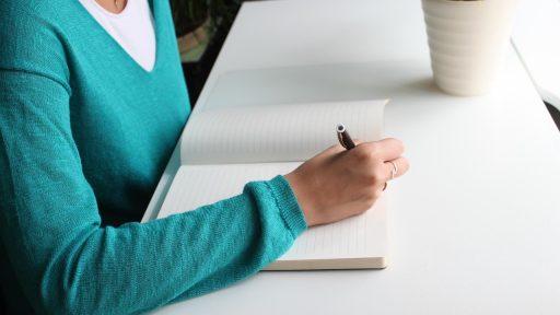 Vrouw schrijft aantekeningen in notitieboek aan bureau