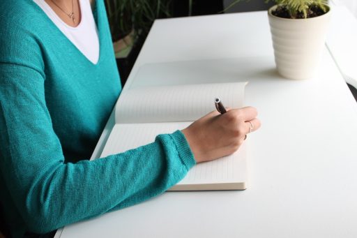 Vrouw schrijft aantekeningen in notitieboek aan bureau