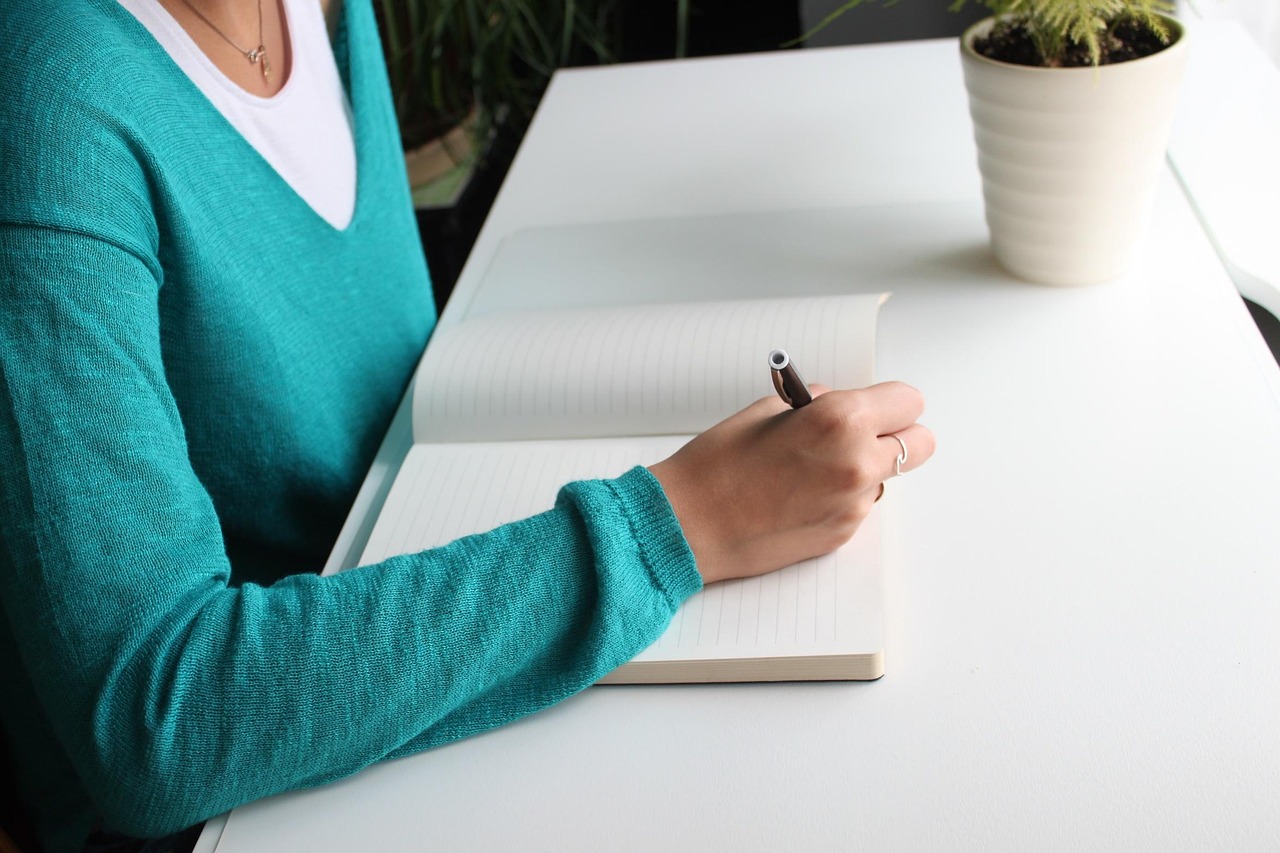 Vrouw schrijft aantekeningen in notitieboek aan bureau