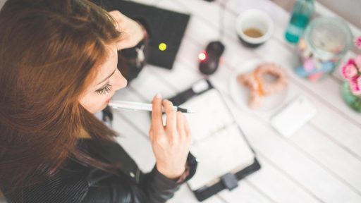 Vrouw achter haar bureau op kantoor die nadenkend voor zich uitkijkt