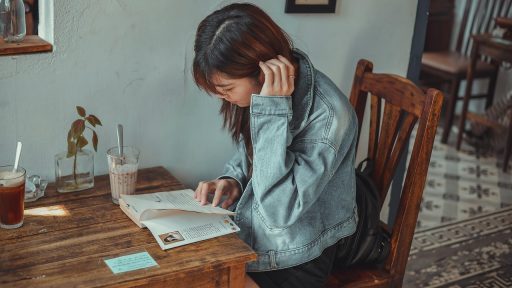 Een vrouw leest een boek aan een tafeltje in een rustig café