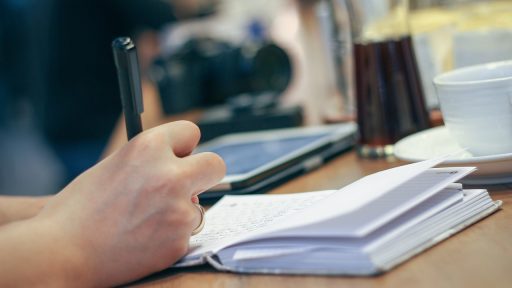 Vrouw schrijft in een notitieboekje aan een tafel terwijl ze haar persoonlijke doelen op een rij zet