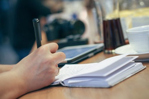 Vrouw schrijft in een notitieboekje aan een tafel terwijl ze haar persoonlijke doelen op een rij zet