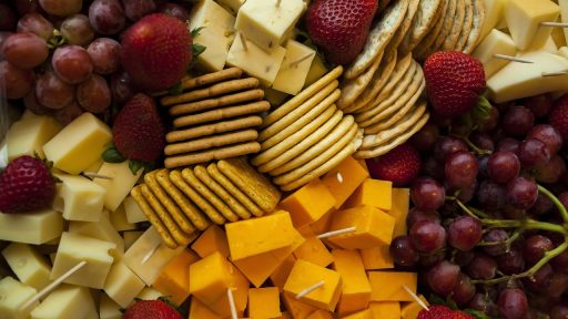 Een kleurrijk plateau met gezonde traktaties zoals vers fruit, rijstwafels, hummus en stukjes pure chocolade op een kantoorbureau