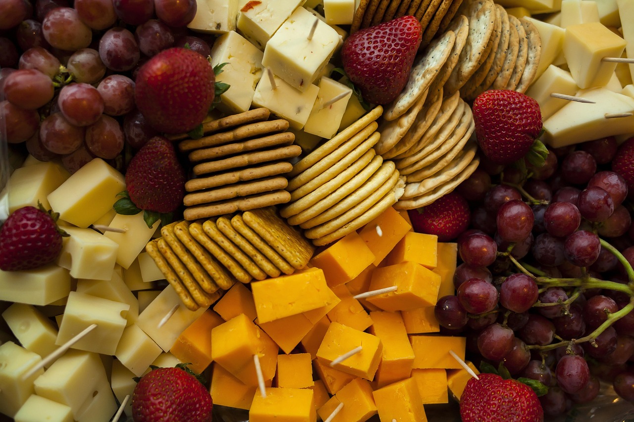 Een kleurrijk plateau met gezonde traktaties zoals vers fruit, rijstwafels, hummus en stukjes pure chocolade op een kantoorbureau